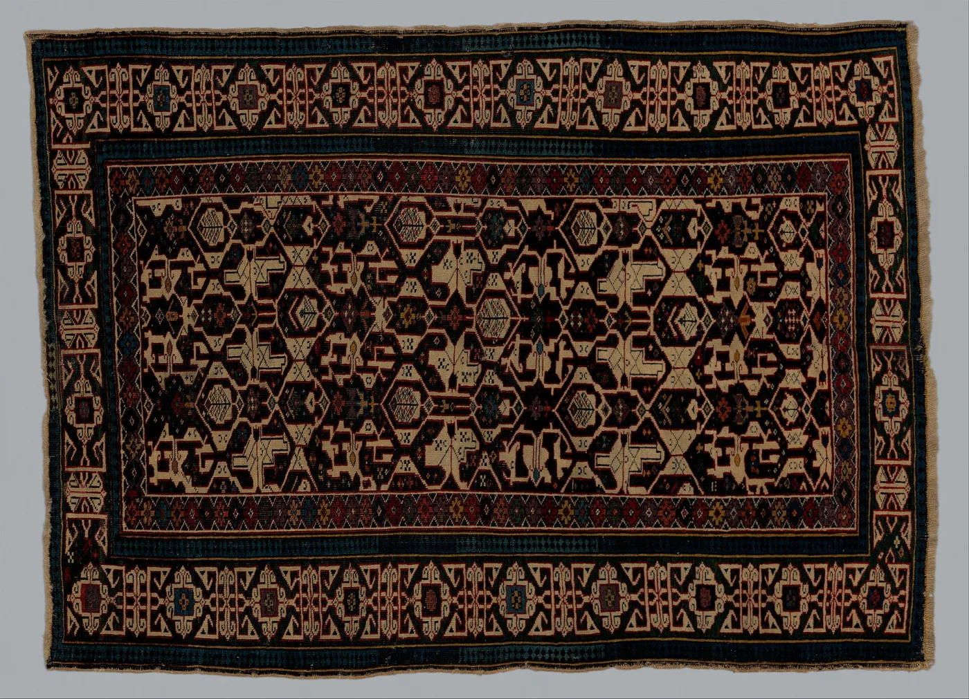 Late nineteenth century Shirvan rug with a dark field carrying a lattice of small angular motifs, framed by a border of blocky angular devices derived from Kufic script