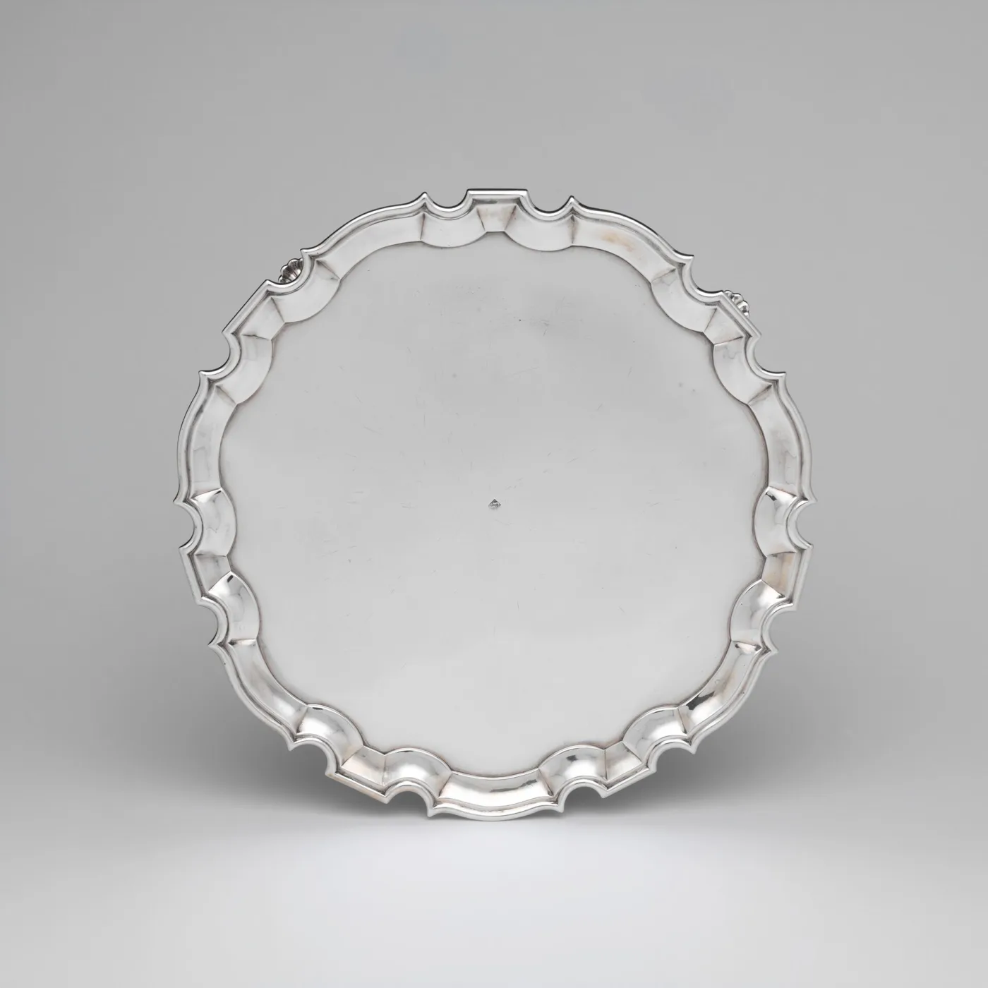 Circular silver salver with a plain polished centre and a moulded shaped rim of alternating curves and points, standing slightly above the surface