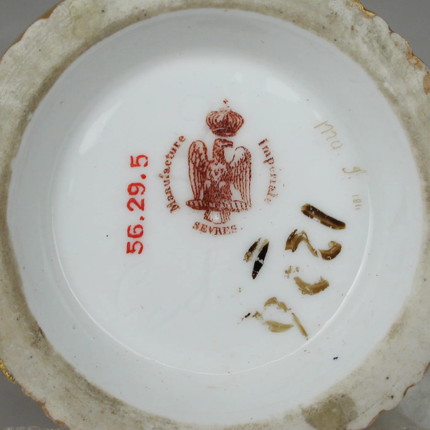 Underside of a Sèvres saucer printed in red with a crowned imperial eagle and the words Manufacture Impériale Sèvres, with gold decorators' marks and a red museum number alongside