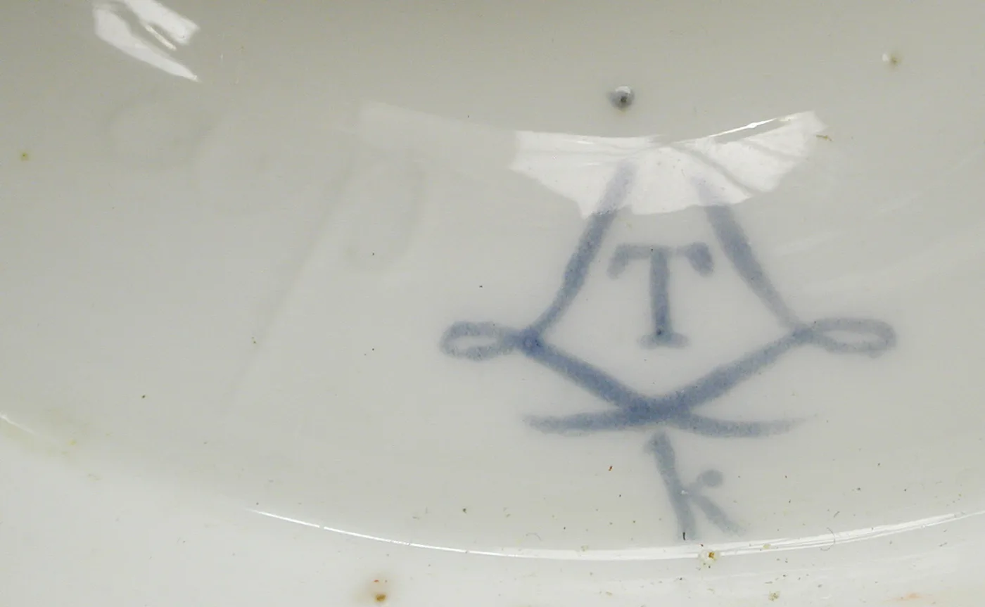 Underglaze blue interlaced-L cipher enclosing the letter T with a small lower-case k below, painted on a curved white surface