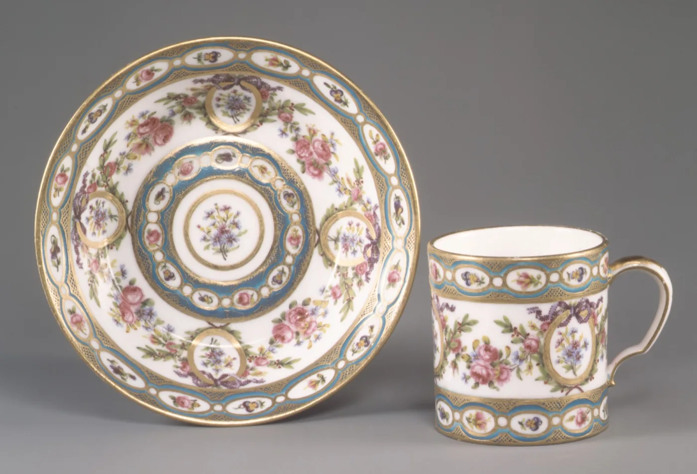 Cylindrical Sèvres coffee can and its saucer, with turquoise and gilt bands enclosing small oval floral medallions