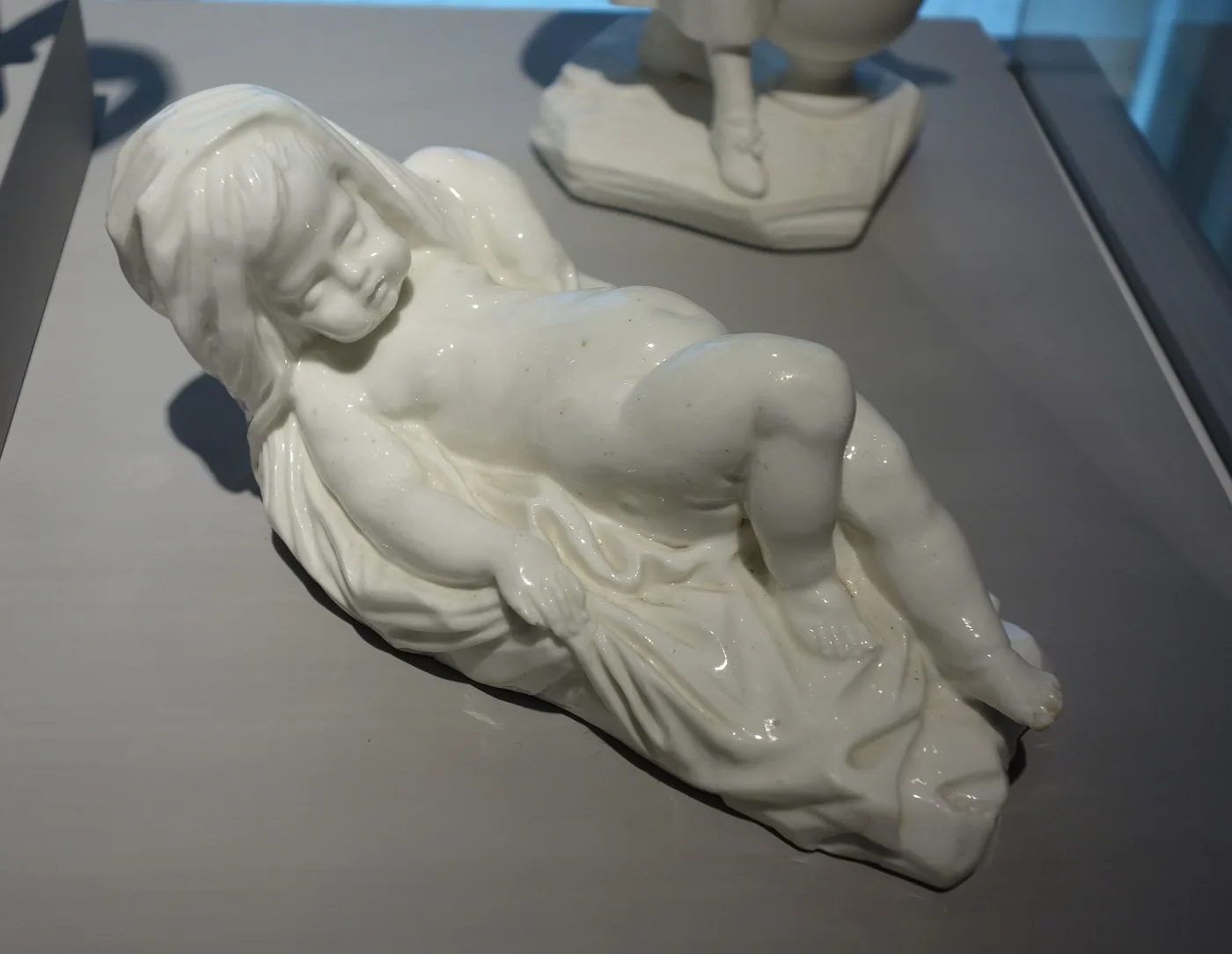 Glazed white porcelain figure of a sleeping child lying on folds of drapery