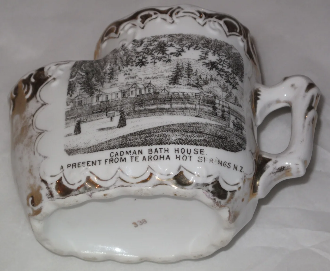 White china shaving mug with gold edging and a black-and-white transfer print of women playing tennis, the rim moulded with a pierced soap drainer