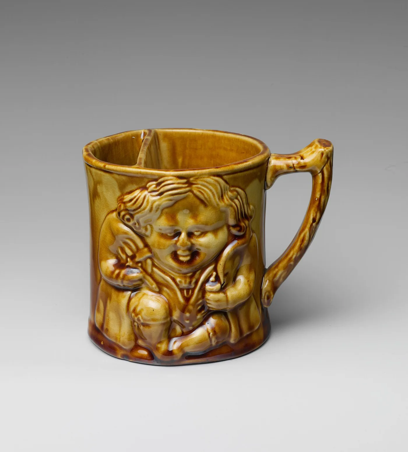 Mottled brown glazed pottery shaving mug moulded in relief with two cherub figures flanking the body, with a loop handle