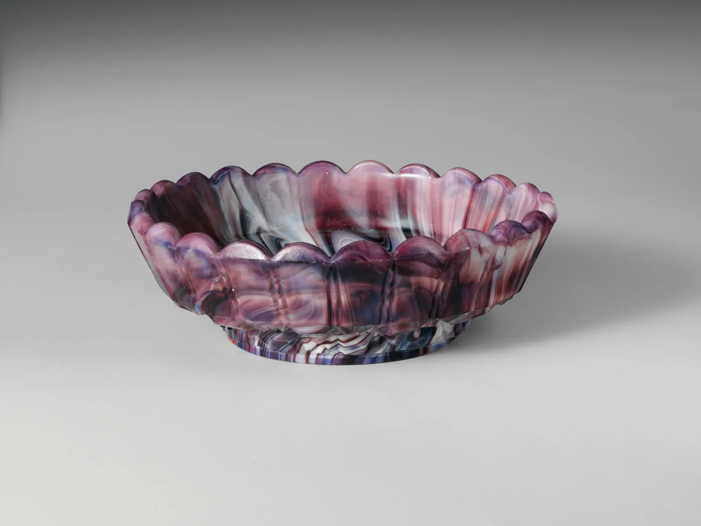 Shallow scalloped purple and white marbled glass dish seen from the side, the marbling visible through the thickness of the scalloped wall