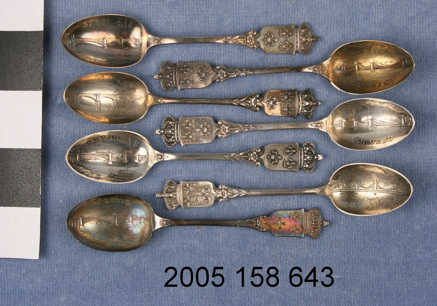 Seven identical demitasse souvenir spoons showing markedly different degrees of tarnish, one handle with strong iridescent colour