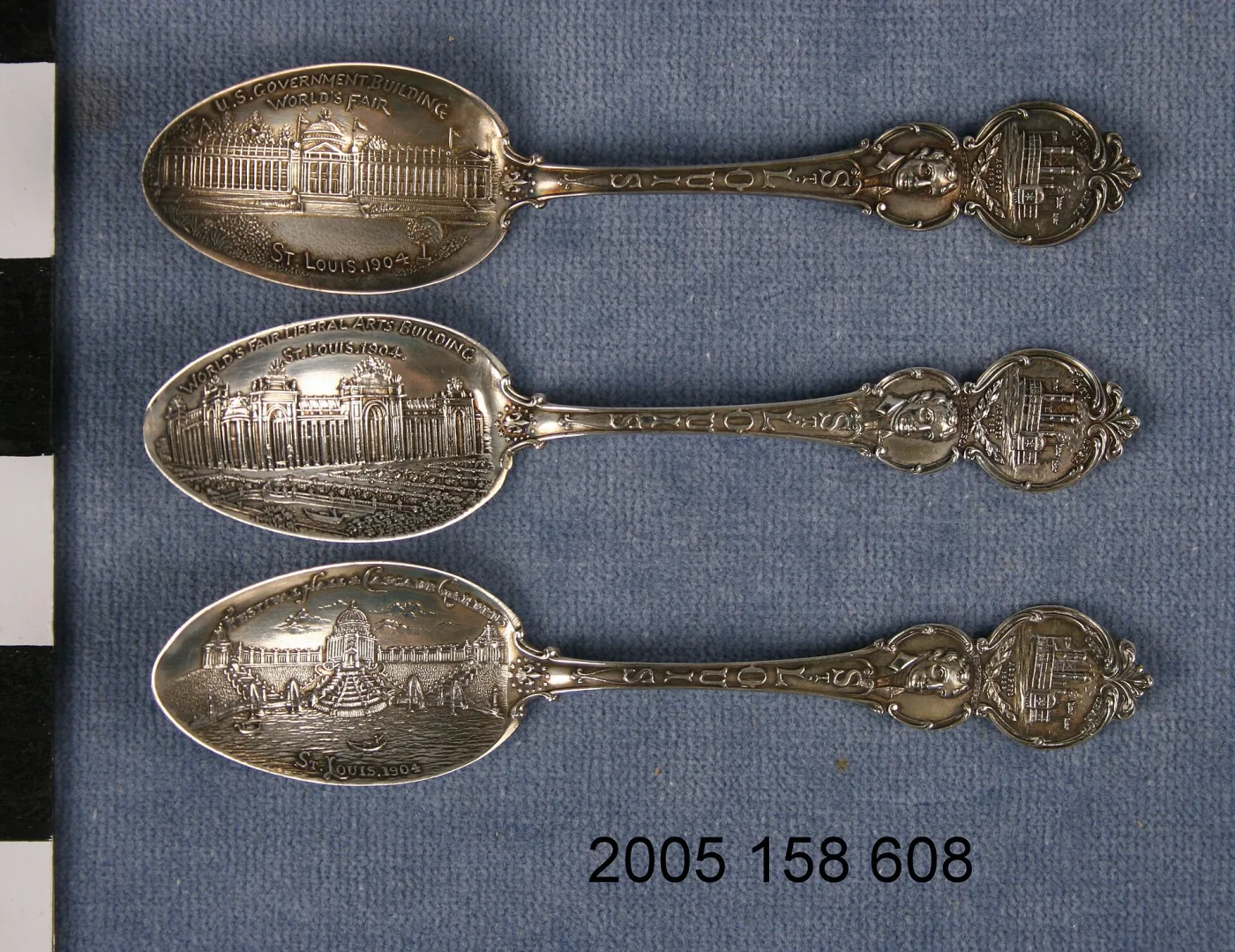 Three silver souvenir teaspoons side by side, each bowl embossed with a different 1904 St. Louis World's Fair building and lettered with its name
