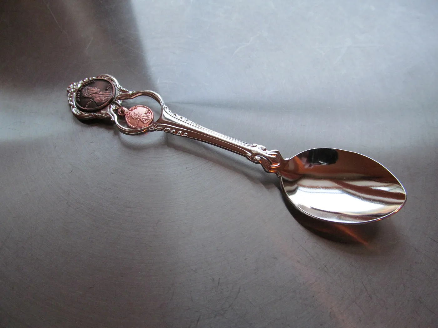 Mirror-bright modern souvenir spoon with a US one-cent coin set into the handle and a small penny charm hanging beside it