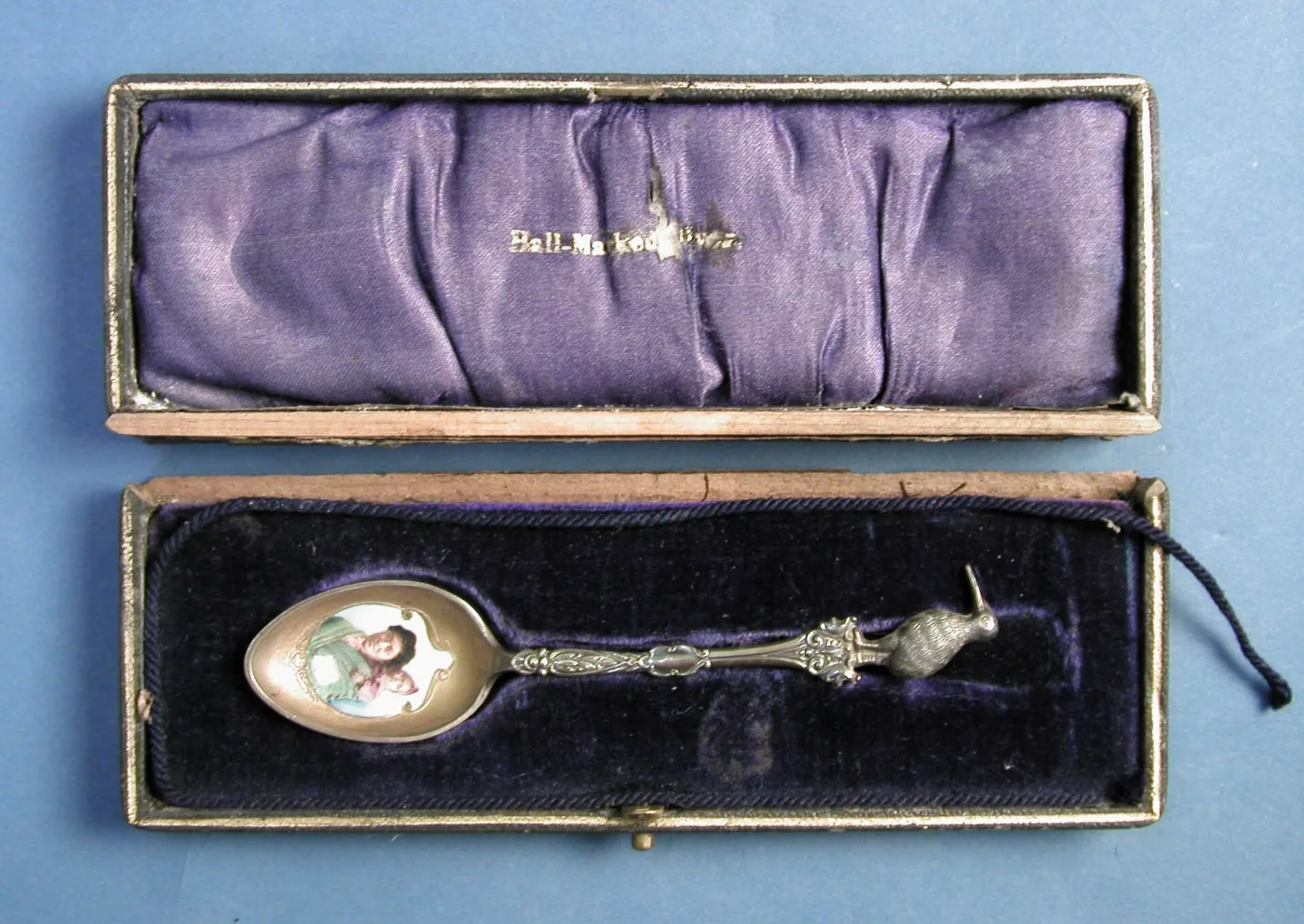 Enamelled souvenir spoon with a cast kiwi finial lying in its original fitted case, the satin lid printed Hall-Marked Silver