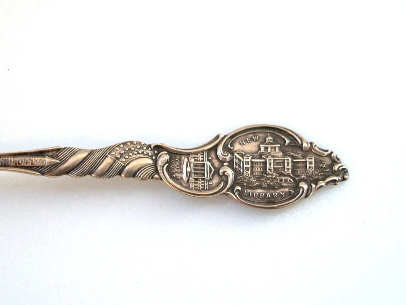 Magnified spoon finial showing two cartouches labelled WHITE HOUSE and NEW LIBRARY above a twisted stem carrying a US flag