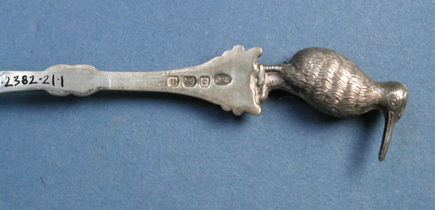 Four small hallmark punches struck in a row on the back of a silver spoon handle below a cast kiwi finial