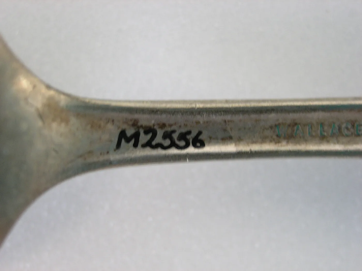 Magnified spoon stem stamped with the maker's name WALLACE, with a museum accession number inked beside it
