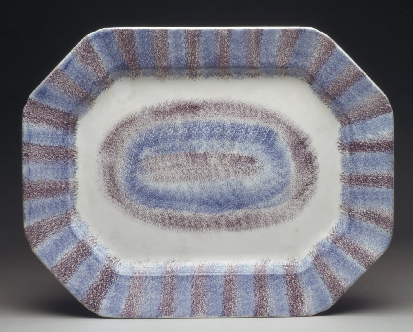 An octagonal platter decorated entirely in alternating bands of blue and purple sponging, radiating around the rim and forming concentric rings in the well, with no painted motif