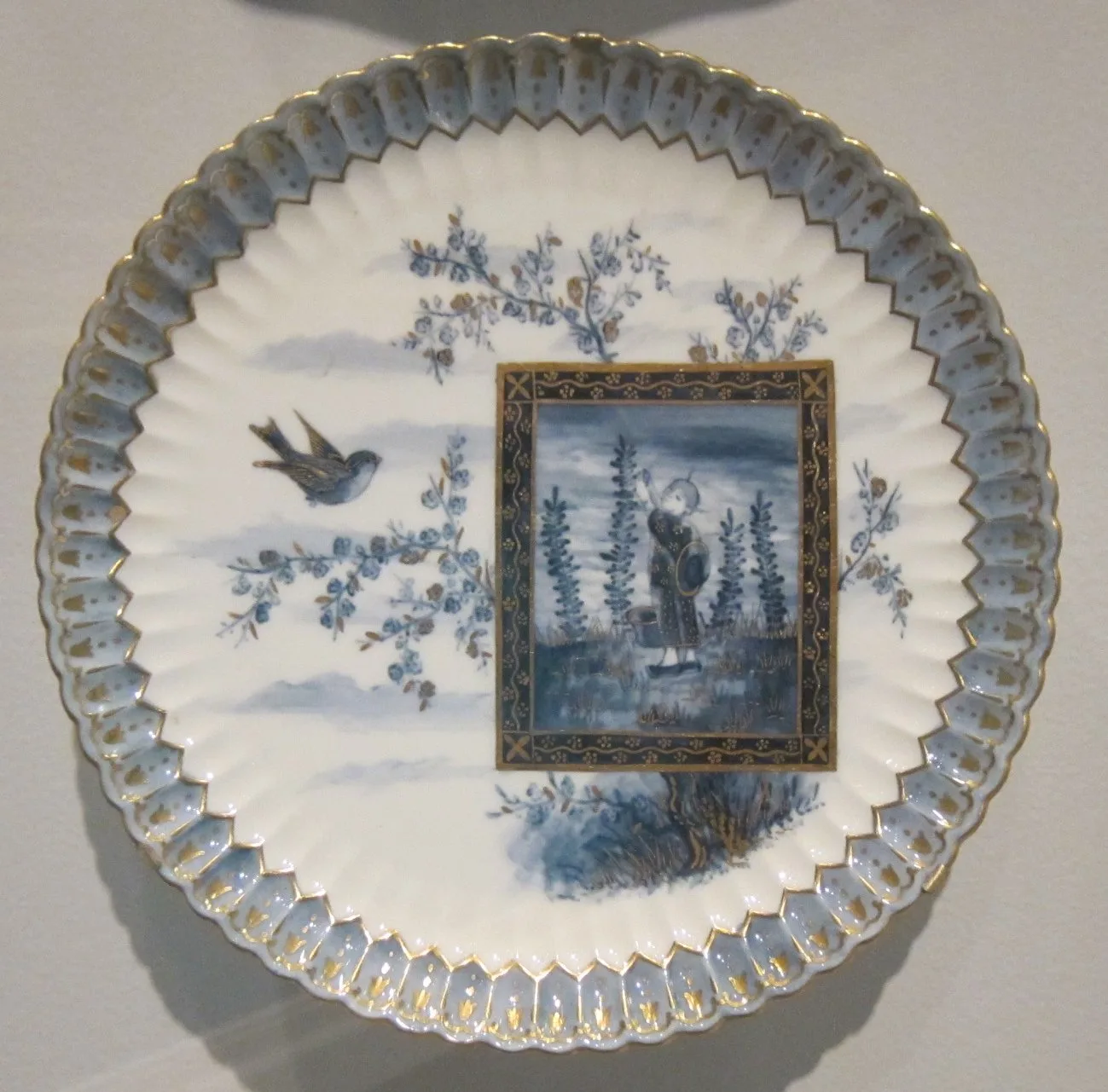 Companion plate of the same late nineteenth-century service, printed in blue with a landscape panel framed in a rectangular gilt border, a flying bird above it and a moulded gadrooned rim