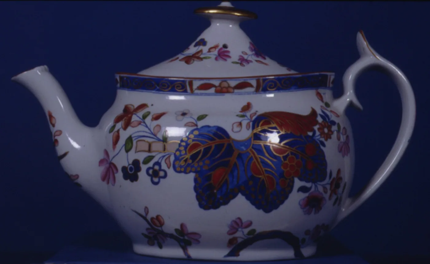 Bute-shaped Spode teapot with its lid, painted in underglaze blue and iron red with a large leaf and rockwork spray, a blue and gilt band round the shoulder and a sharply angled handle