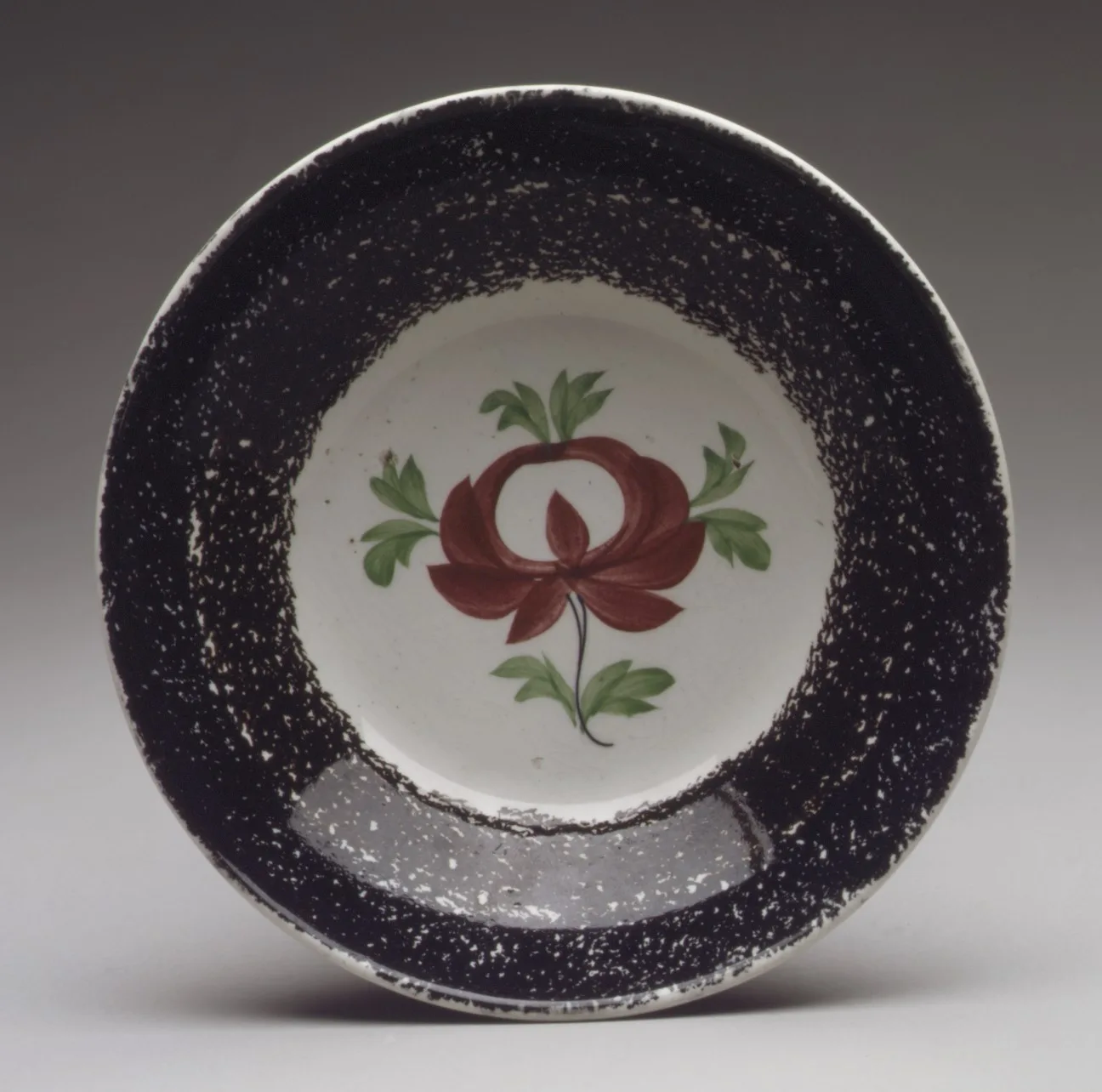 Deep saucer of about 1800 to 1830 with a wide manganese purple spattered border and a hand-painted red rose with green leaves in the white centre