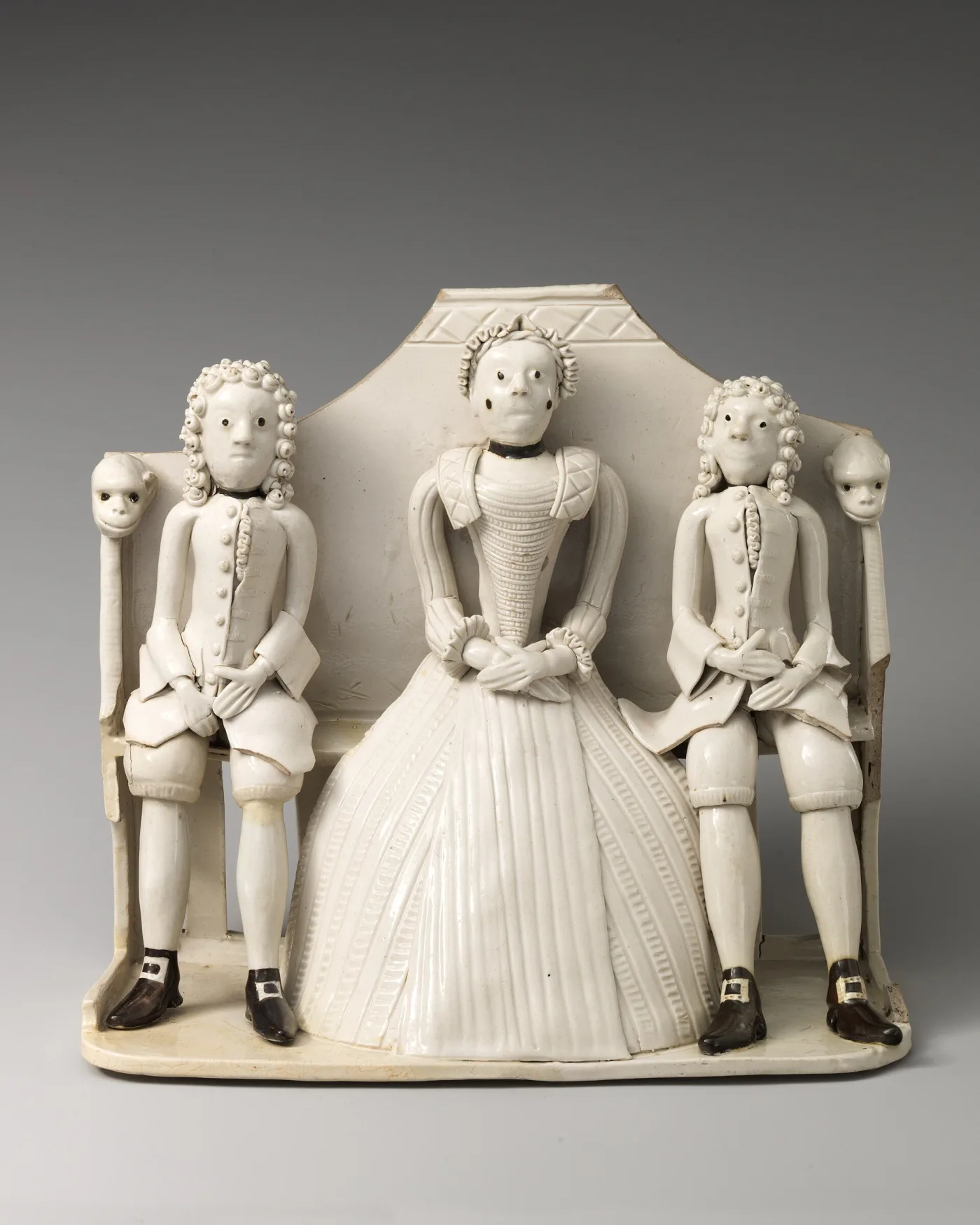 White salt-glazed stoneware group of a woman in a wide panniered dress seated on a settle between two men in curled wigs