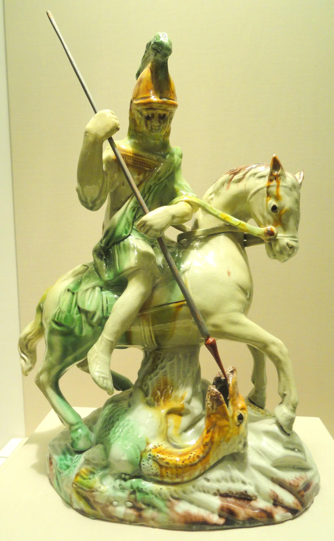 Pottery group of an armoured rider on a pale horse spearing a dragon, glazed in soft green, ochre and cream