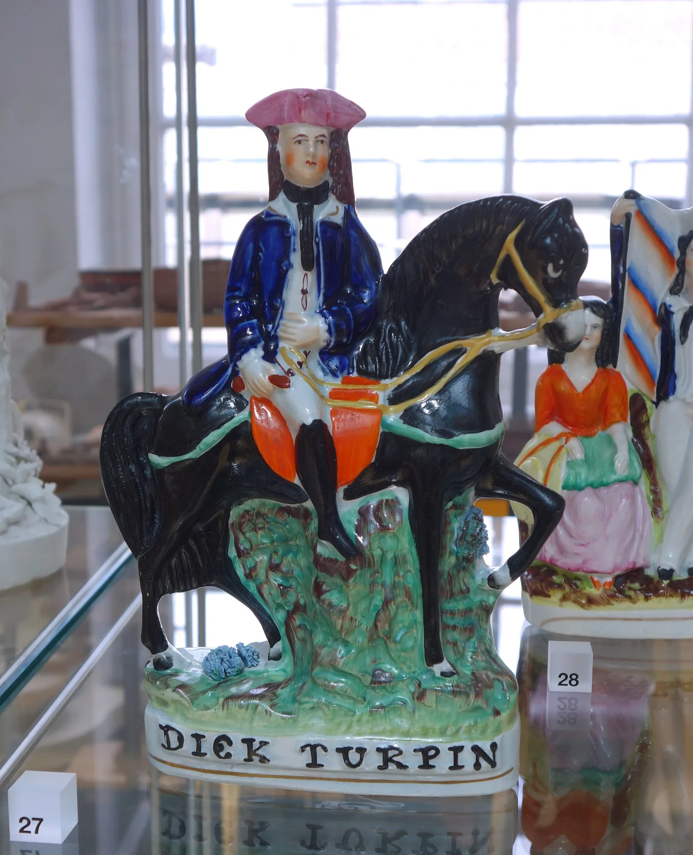 Brightly painted pottery figure of a highwayman in a blue coat on a black horse, the base lettered DICK TURPIN