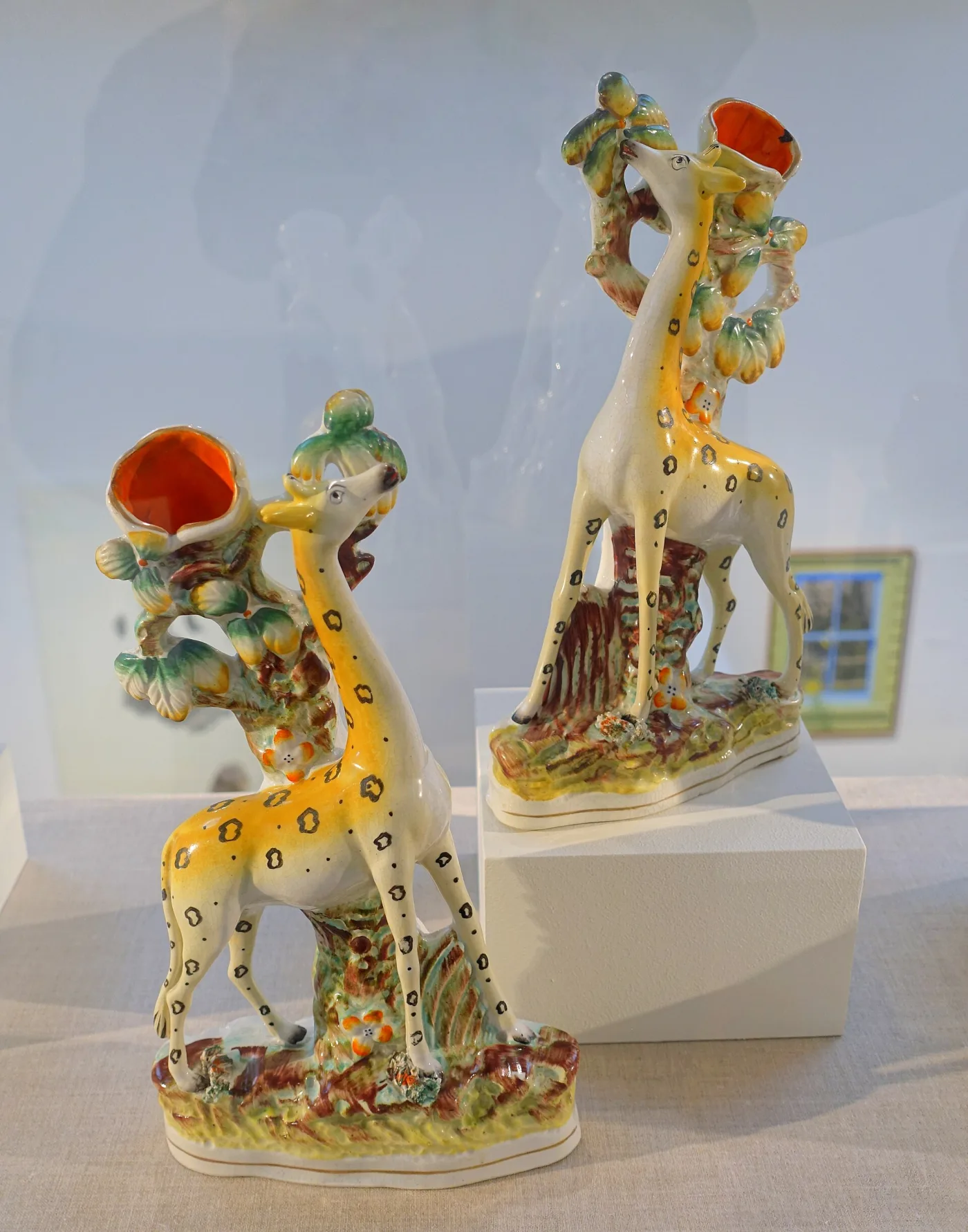 Pair of pottery giraffes standing beside tree stumps, each stump hollowed into an orange-lined opening