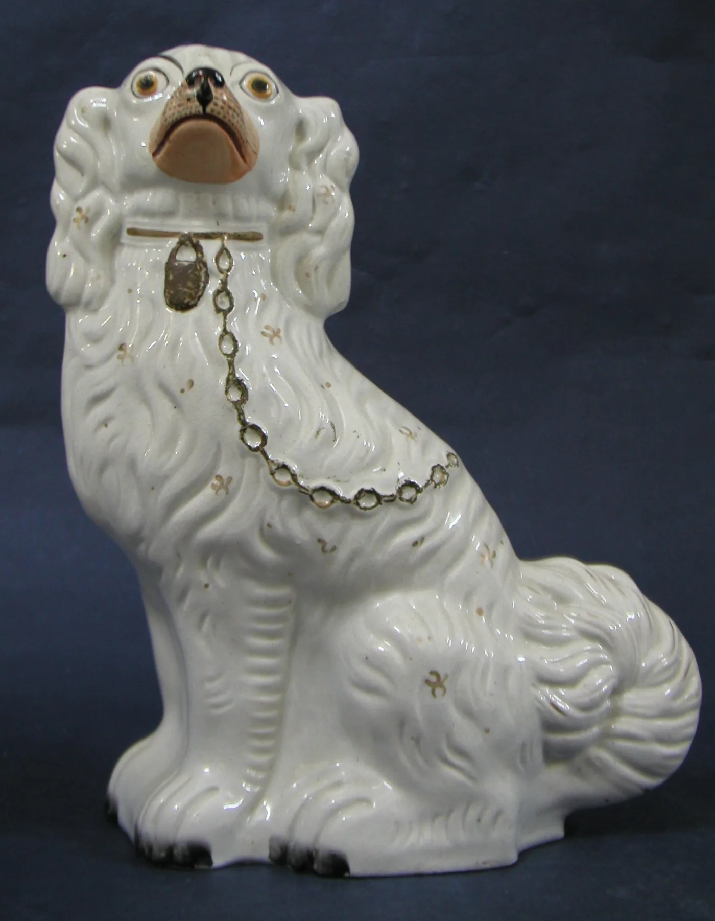 Large white pottery spaniel with a buff-coloured muzzle and a faint, heavily worn gilt chain and padlock