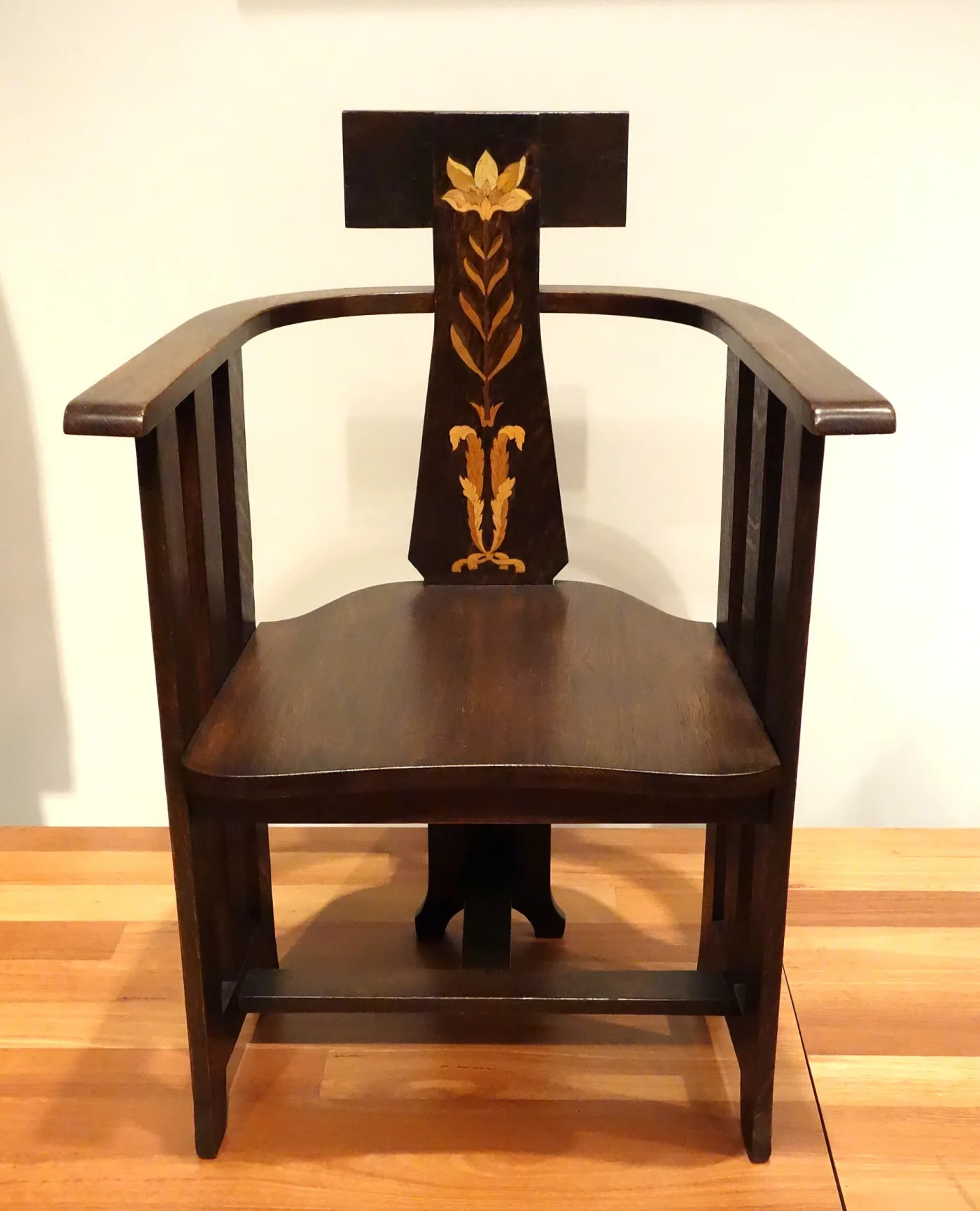 Dark oak armchair with a bowed crest rail, a broad central back splat inlaid with a pale stylised flower, and narrow slats beneath curved arms
