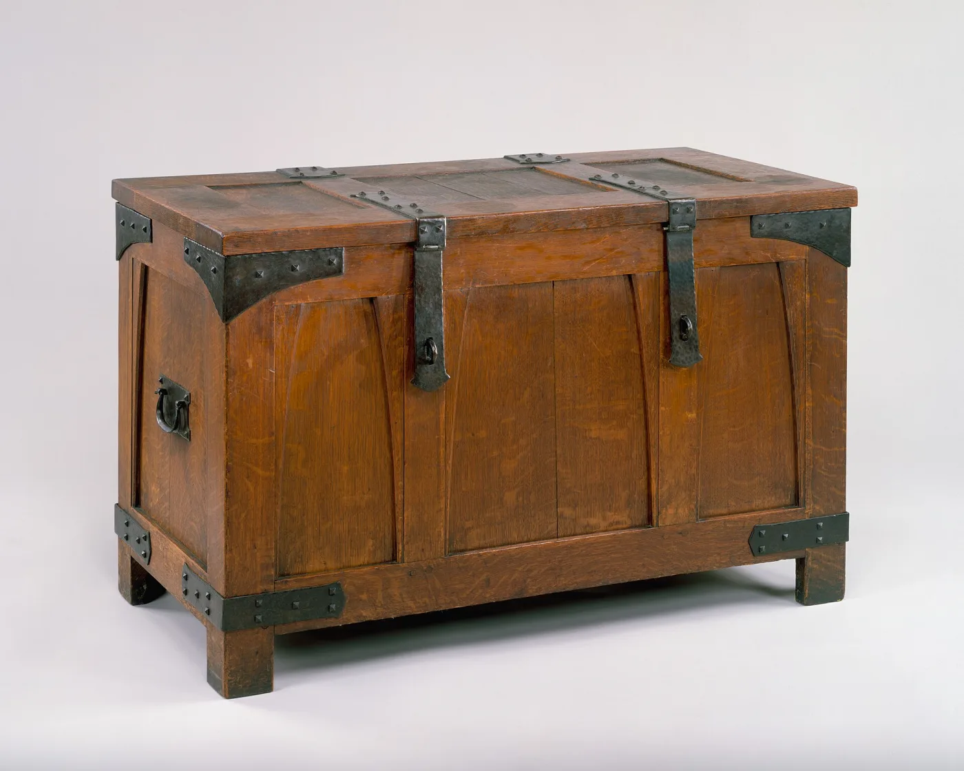 Panelled oak chest with a hinged lid, bound at every corner and along the lid by dark iron straps studded with pyramid-headed rivets, with a ring handle on the end