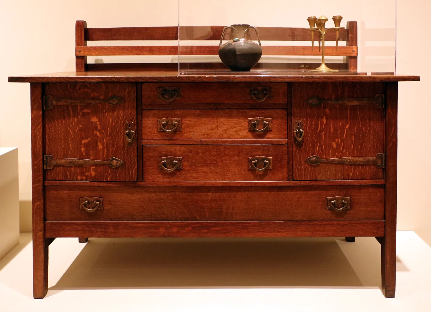 Oak sideboard with a low back rail, three drawers and two cupboard doors, fitted with hammered copper plate pulls with bail handles and long hammered strap hinges