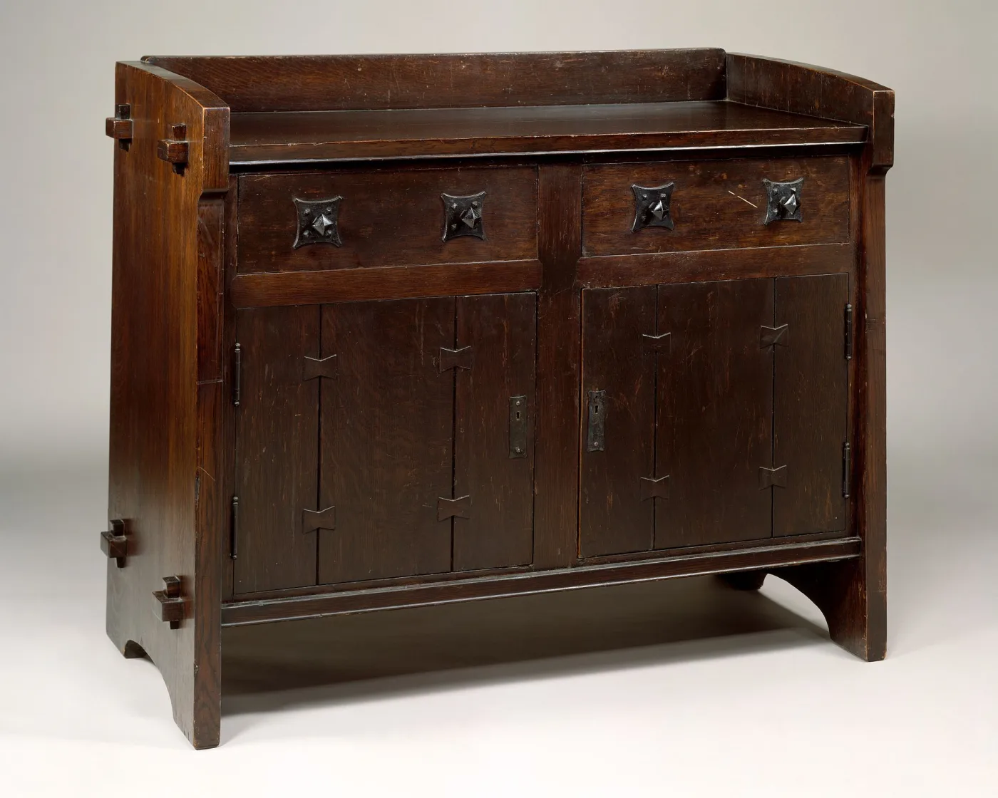 Dark oak side table with a low gallery, two drawers over panelled cupboard doors, square tenon ends projecting from the side stiles and bow-tie keys let into the door panels
