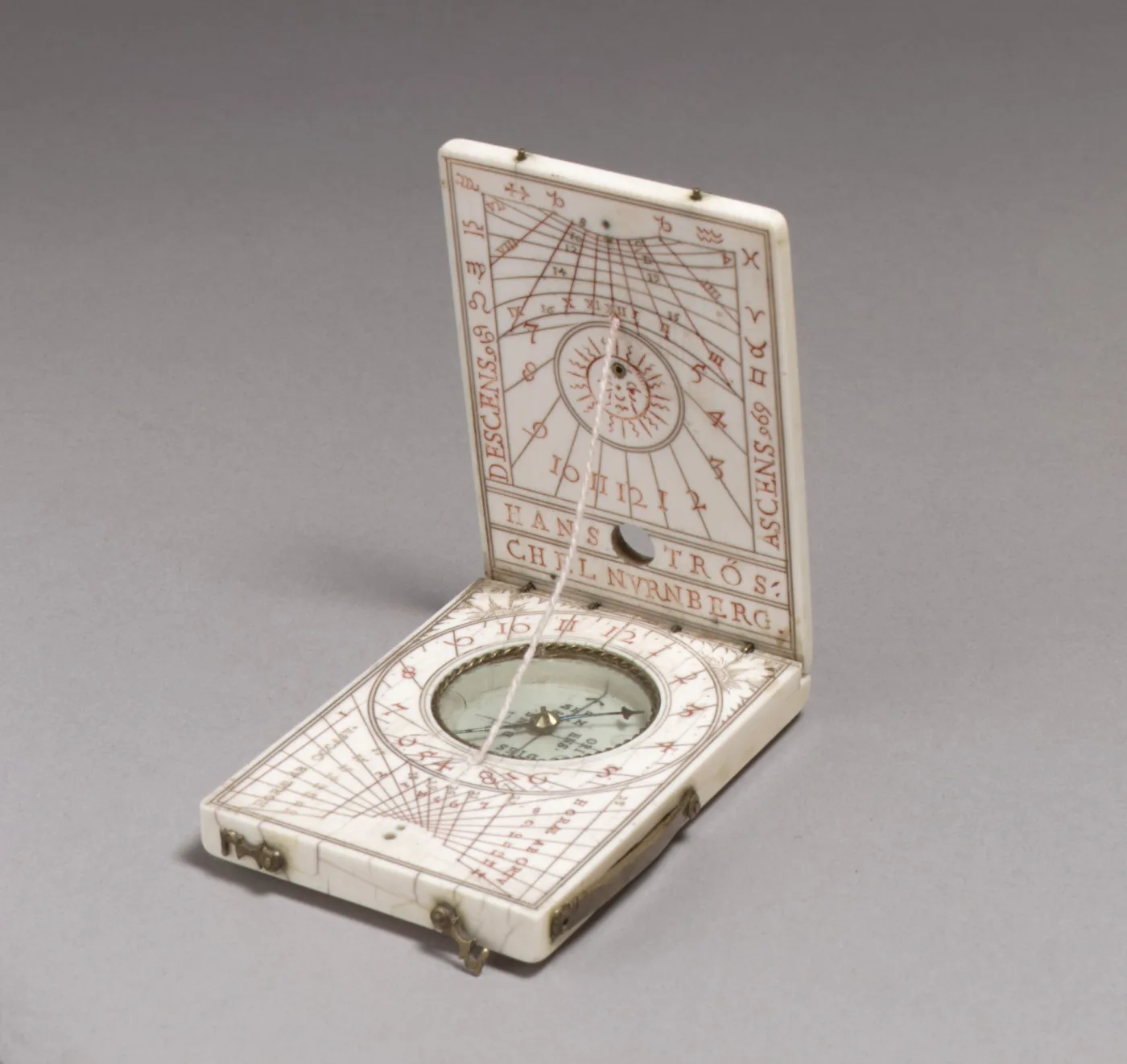 Ivory diptych sundial opened like a book, the upper leaf engraved with hour lines and a face of the sun, a string gnomon running down to a compass set in the lower leaf