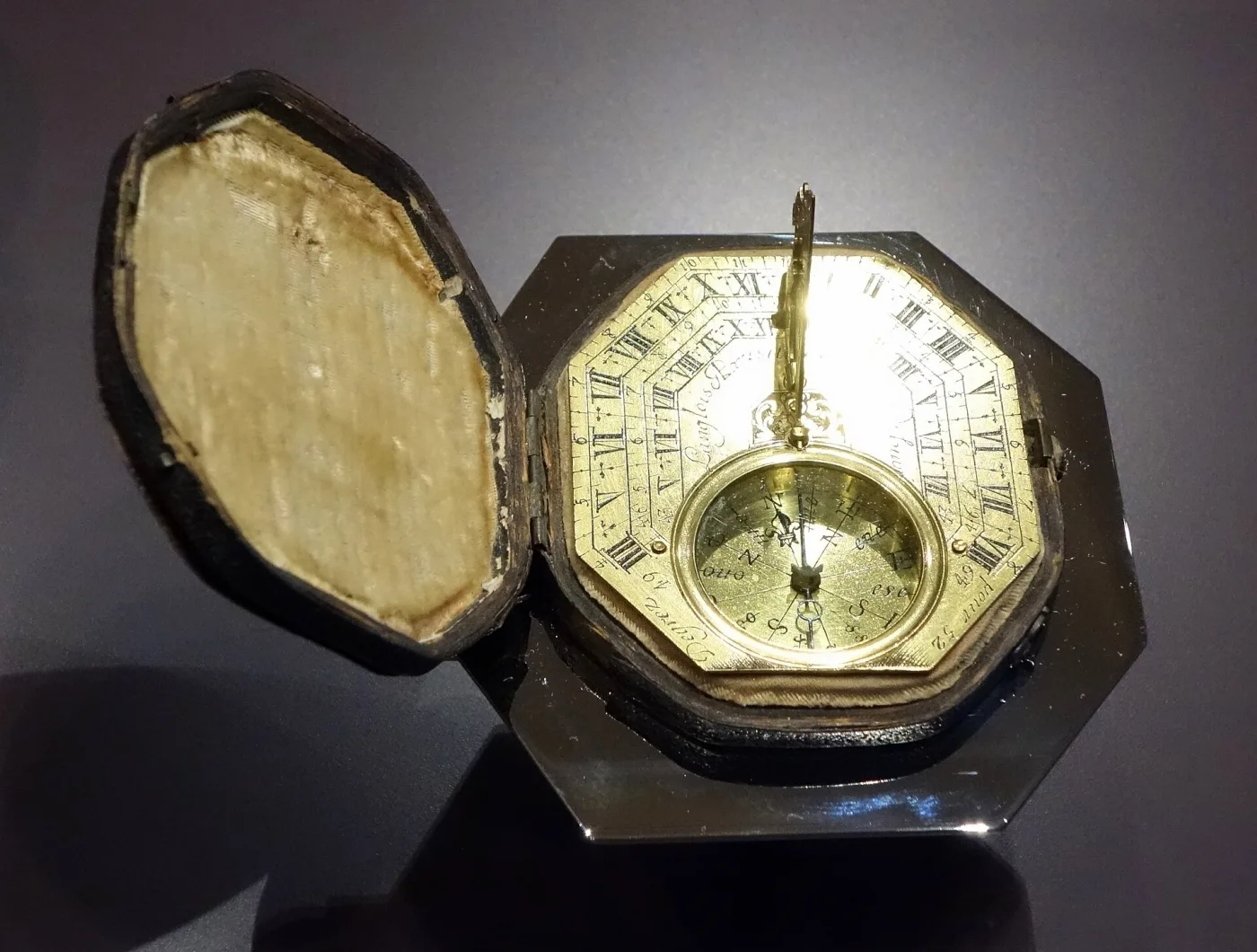 Gilt octagonal pocket sundial with its gnomon raised, sitting in a shaped leather-covered case lined with pale silk, the lid hinged open beside it
