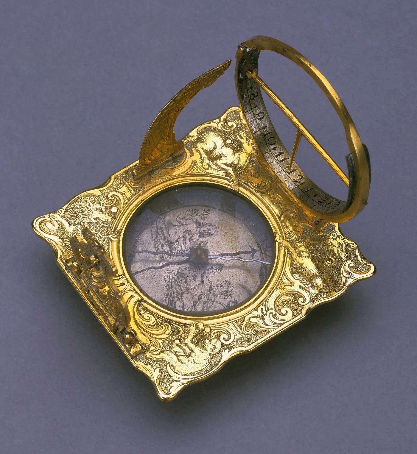 Small gilt-brass portable equatorial sundial with a hinged hour ring standing above a compass, the plate cast with scrolls and animal heads and a folding gnomon blade