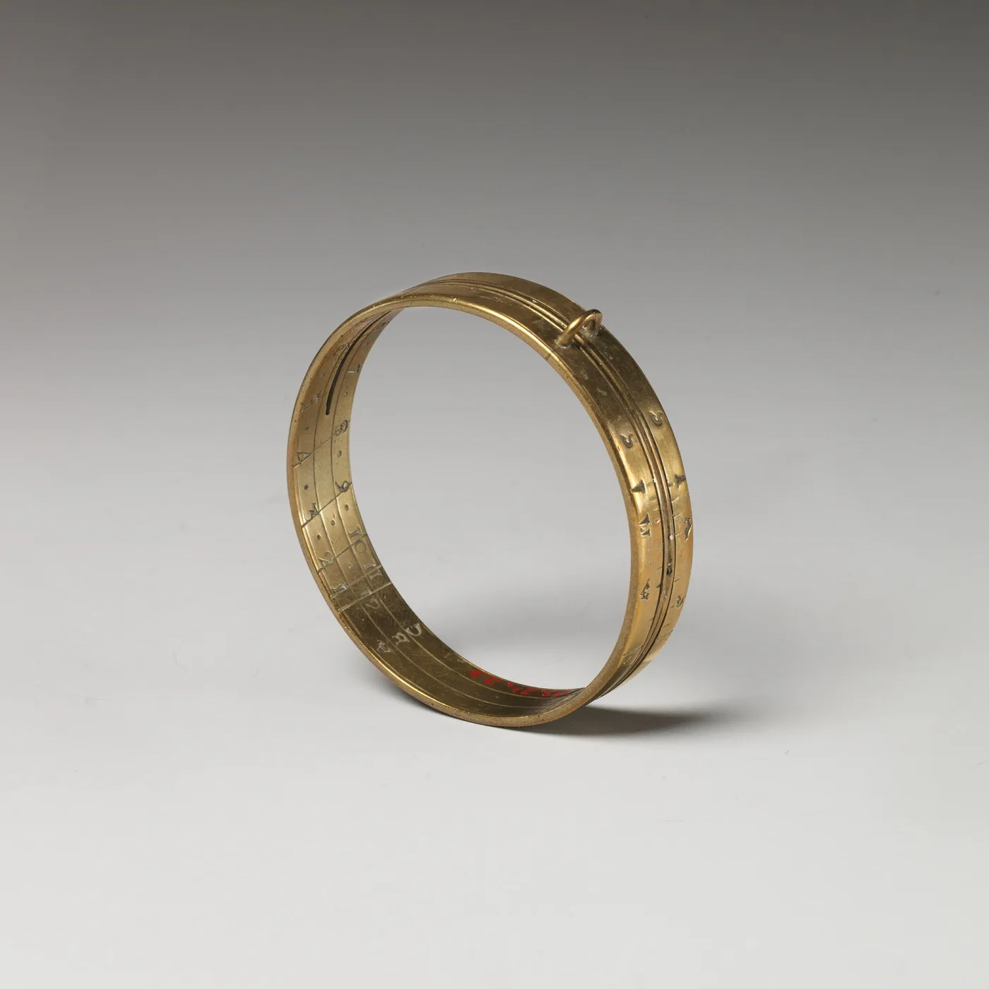 Small plain brass ring dial standing on edge, with a suspension loop and a narrow sliding band pierced by a sighting hole, hour numerals inside the ring