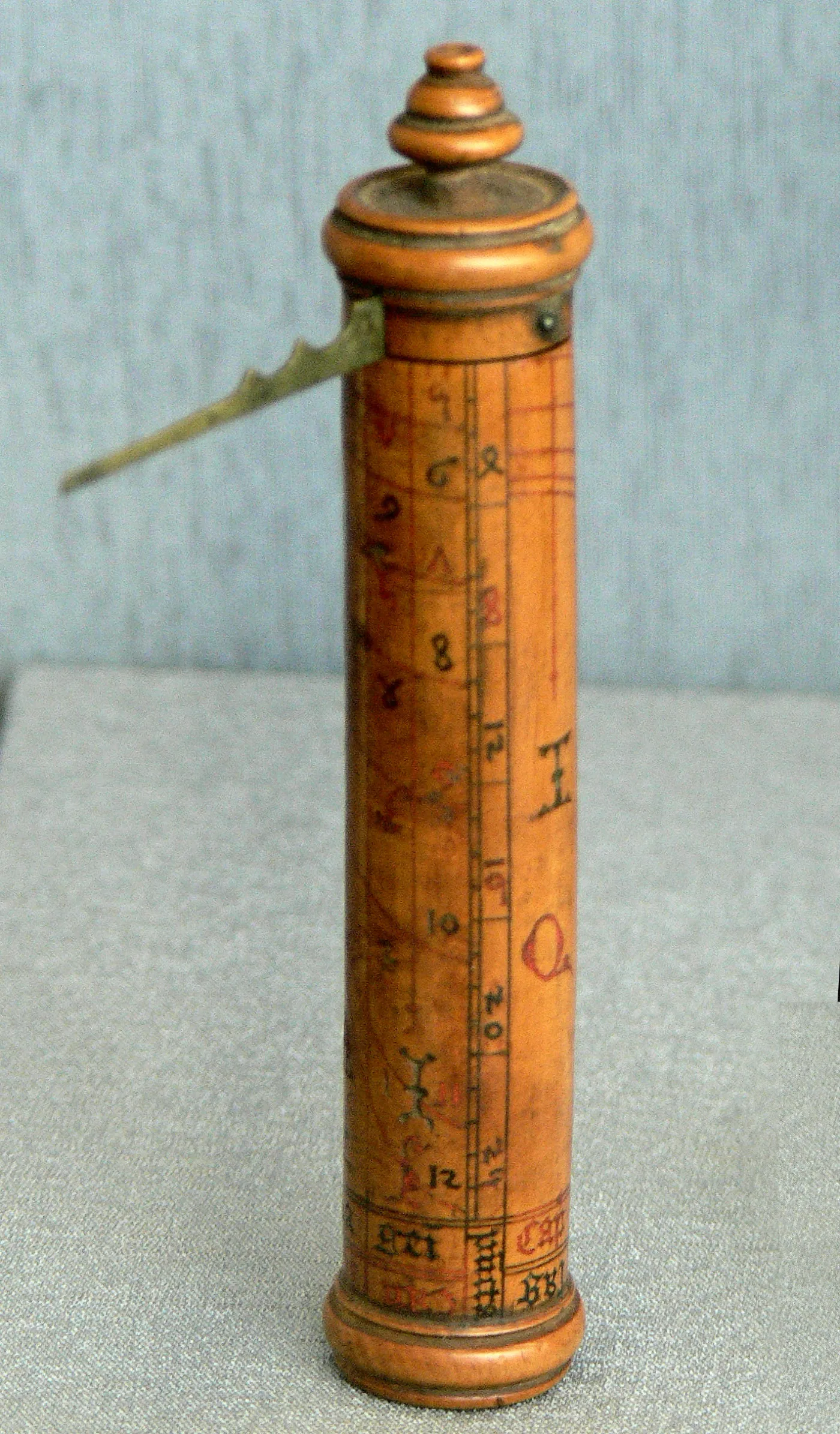 Turned boxwood cylinder sundial with a knopped cap, drawn in red and black with calendar columns and hour curves, a flat brass gnomon swinging out from under the cap