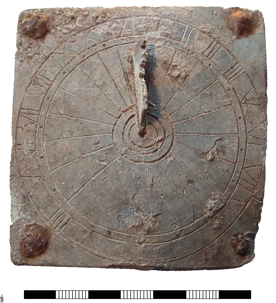 Small square sheet-lead dial plate, heavily corroded, engraved with radiating hour lines, a ring of Roman numerals and a stub of gnomon at the centre, a corroded nail at each corner