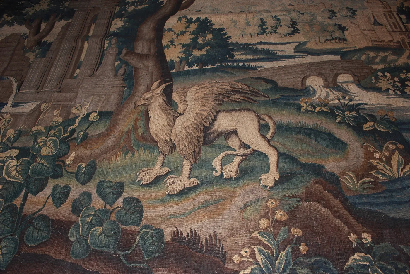 Close detail of a tapestry griffin with an eagle's head and wings and a lion's hindquarters, crouching by a tree, the surrounding foliage faded from green to blue and brown
