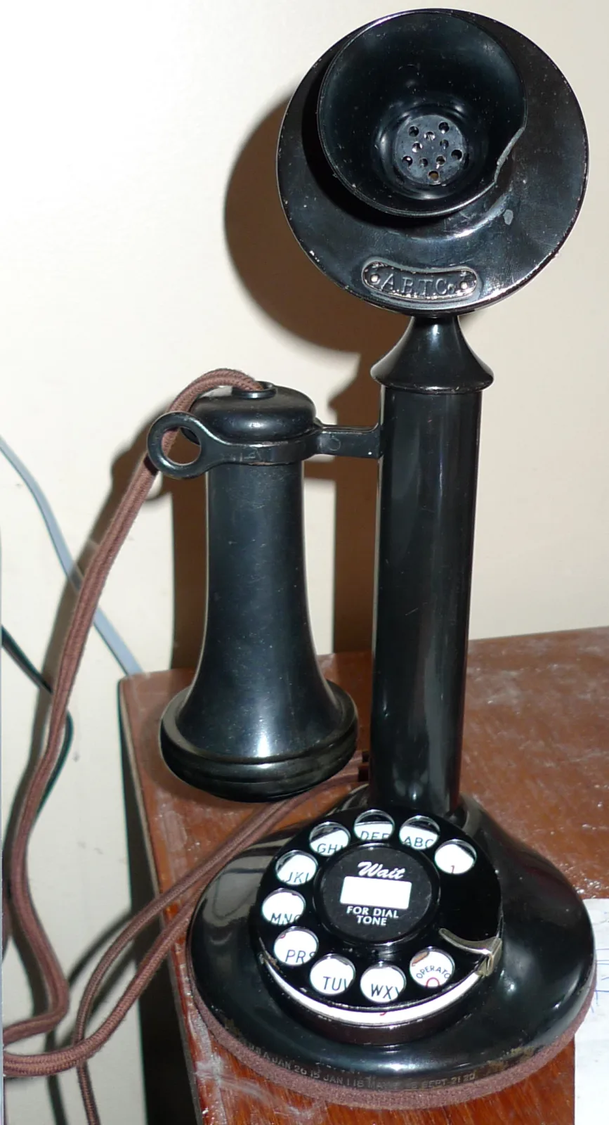 Western Electric candlestick telephone with a black cylindrical column on a round weighted base, a cup transmitter at the top, a receiver hanging on a side hook, and a rotary dial mounted on the base