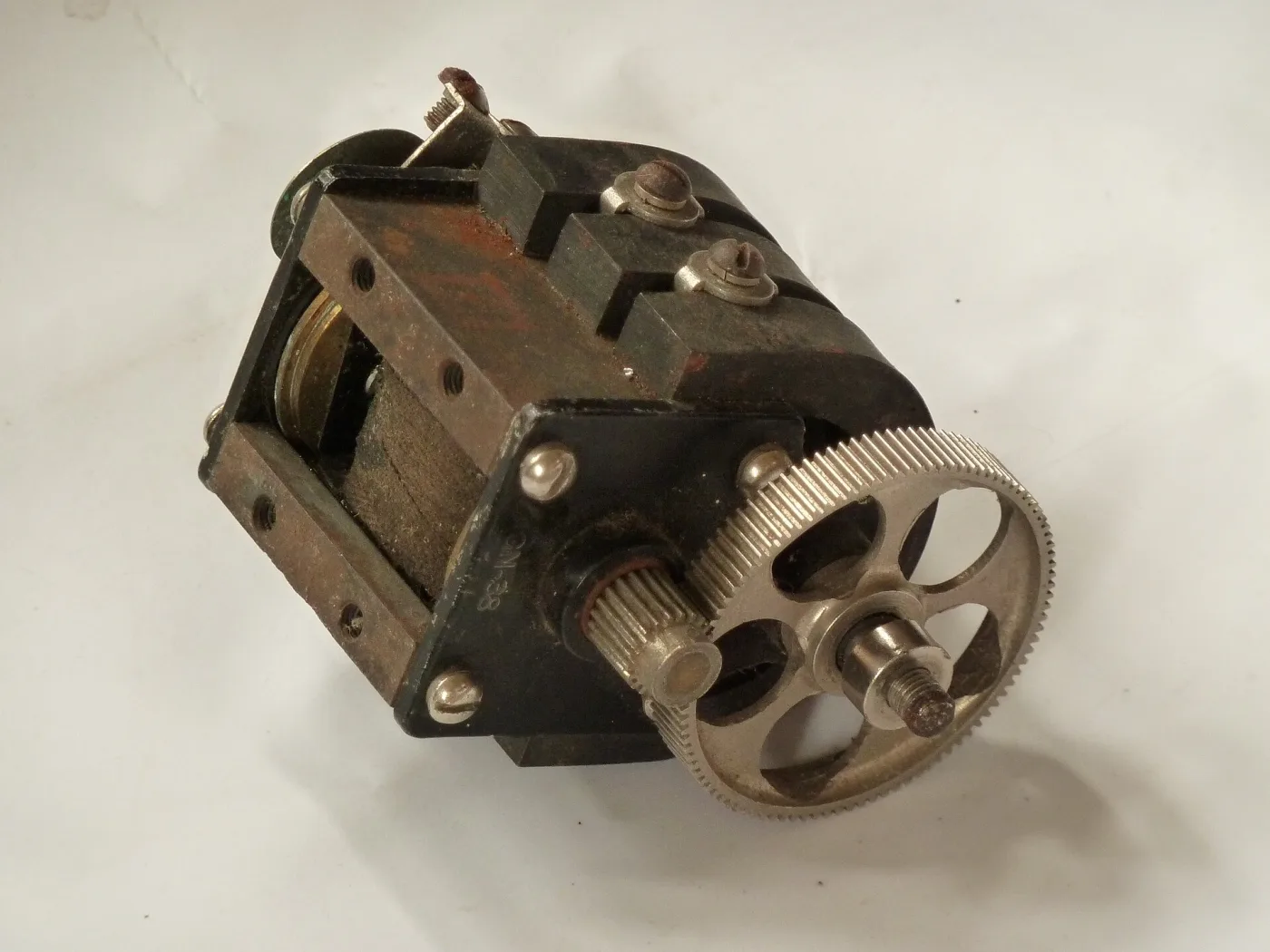 Telephone magneto generator removed from its case and photographed from beneath, showing the horseshoe permanent magnets, the wound armature between them and the brass gear train driven by the crank shaft