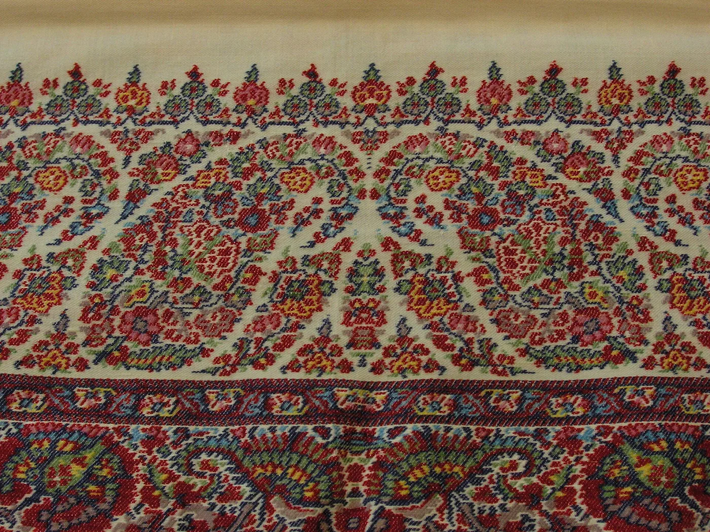 Detail of a woven paisley shawl in Kashmir style, densely patterned with rows of curving boteh motifs in red, blue, green and cream against a dark ground