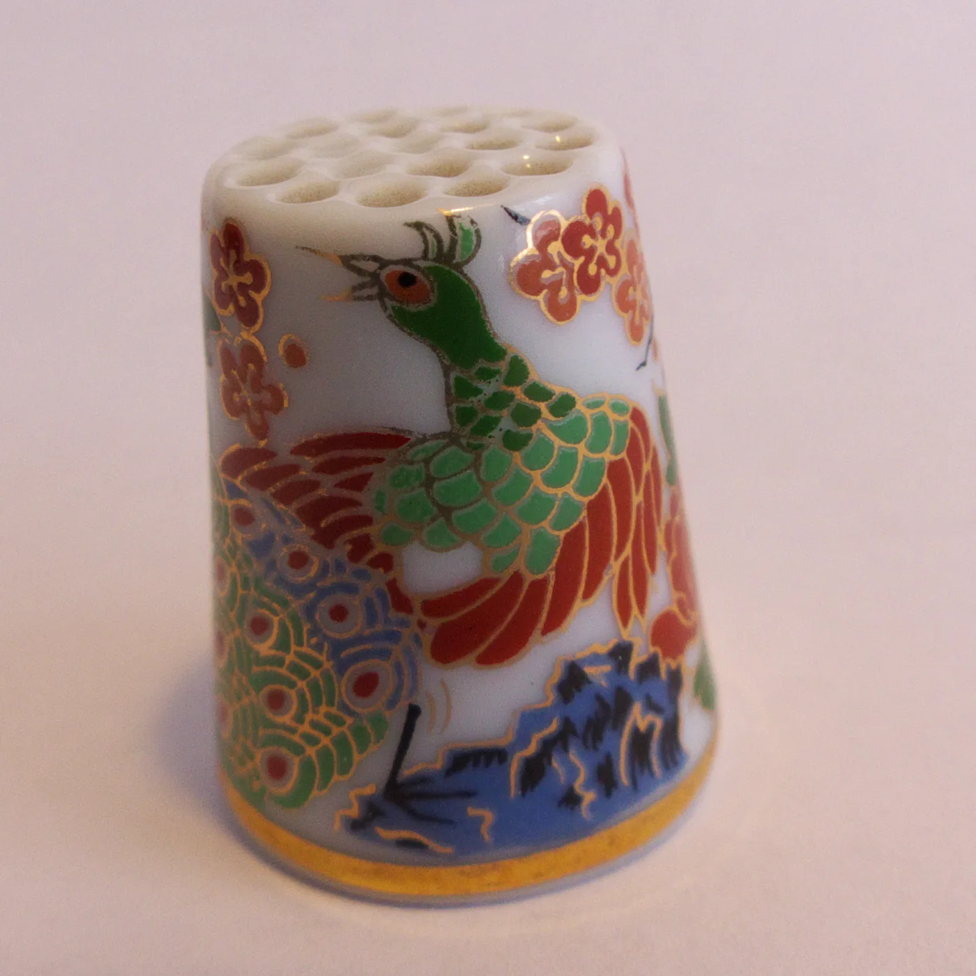 Porcelain thimble painted with a dragon and stylised flowers in red, blue, green and gold, its top pierced with a regular grid of small moulded dimples