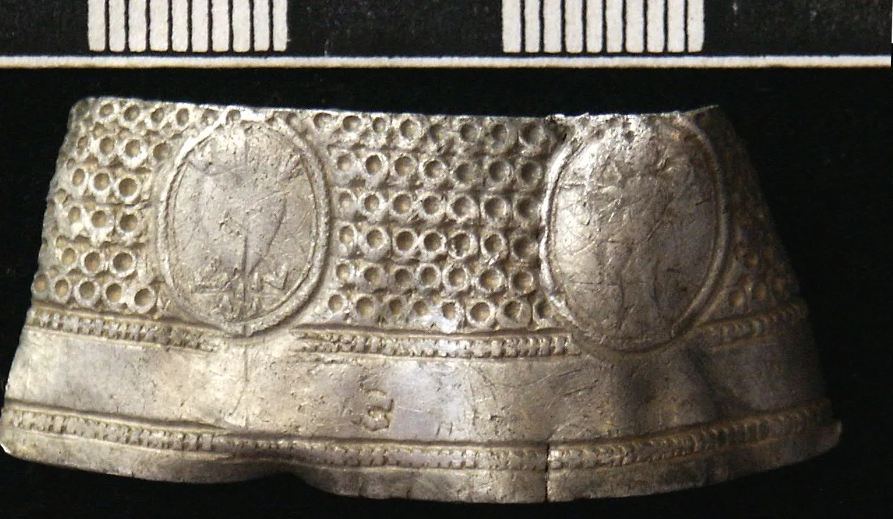 Close view of the decorated band of a seventeenth-century silver thimble, showing a frieze of punched motifs between plain borders below a field of small circular indentations