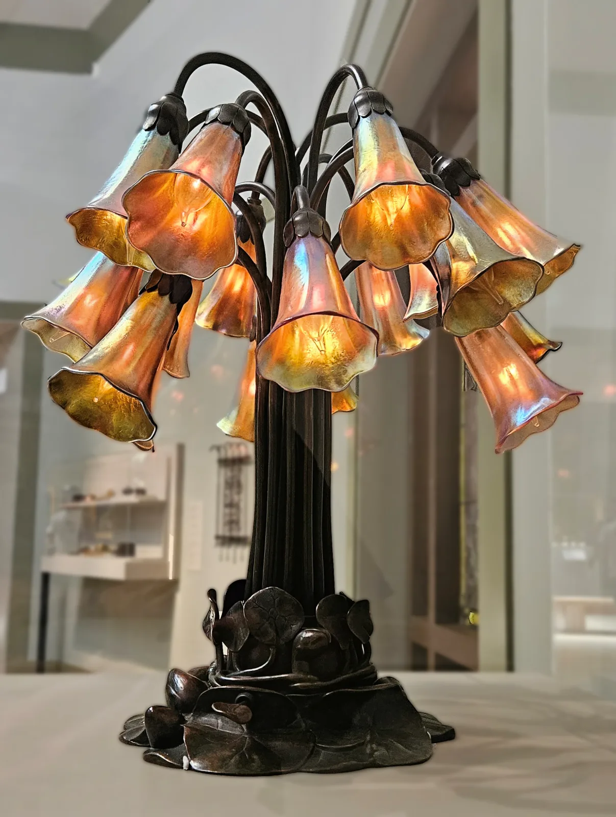 Eighteen-light lily lamp photographed from below, its patinated bronze stems curving up and outward from a lobed lily-pad base, each ending in a downturned glass flower shade