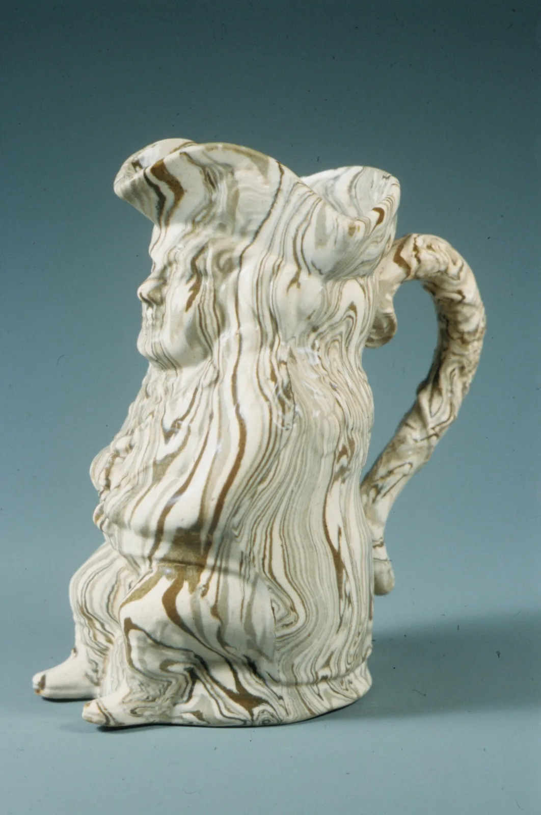 Seated Toby jug of a man in a tricorn hat, the body made of marbled clays swirled together in cream, brown and grey rather than glazed over a single colour