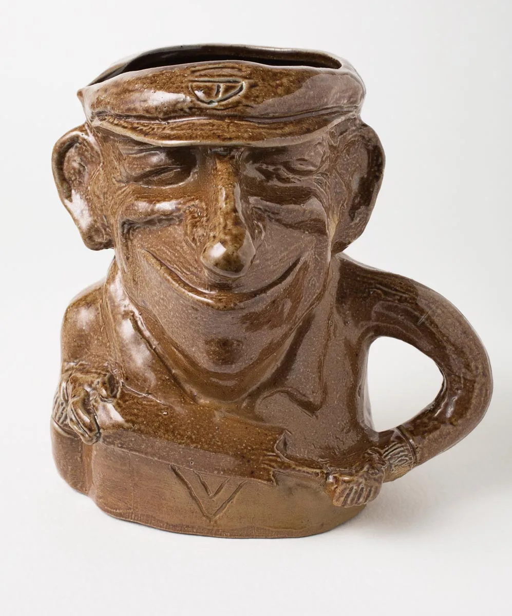 Brown slip-cast character jug of a cricketer in a baggy green cap, the handle formed as a cricket bat and ball
