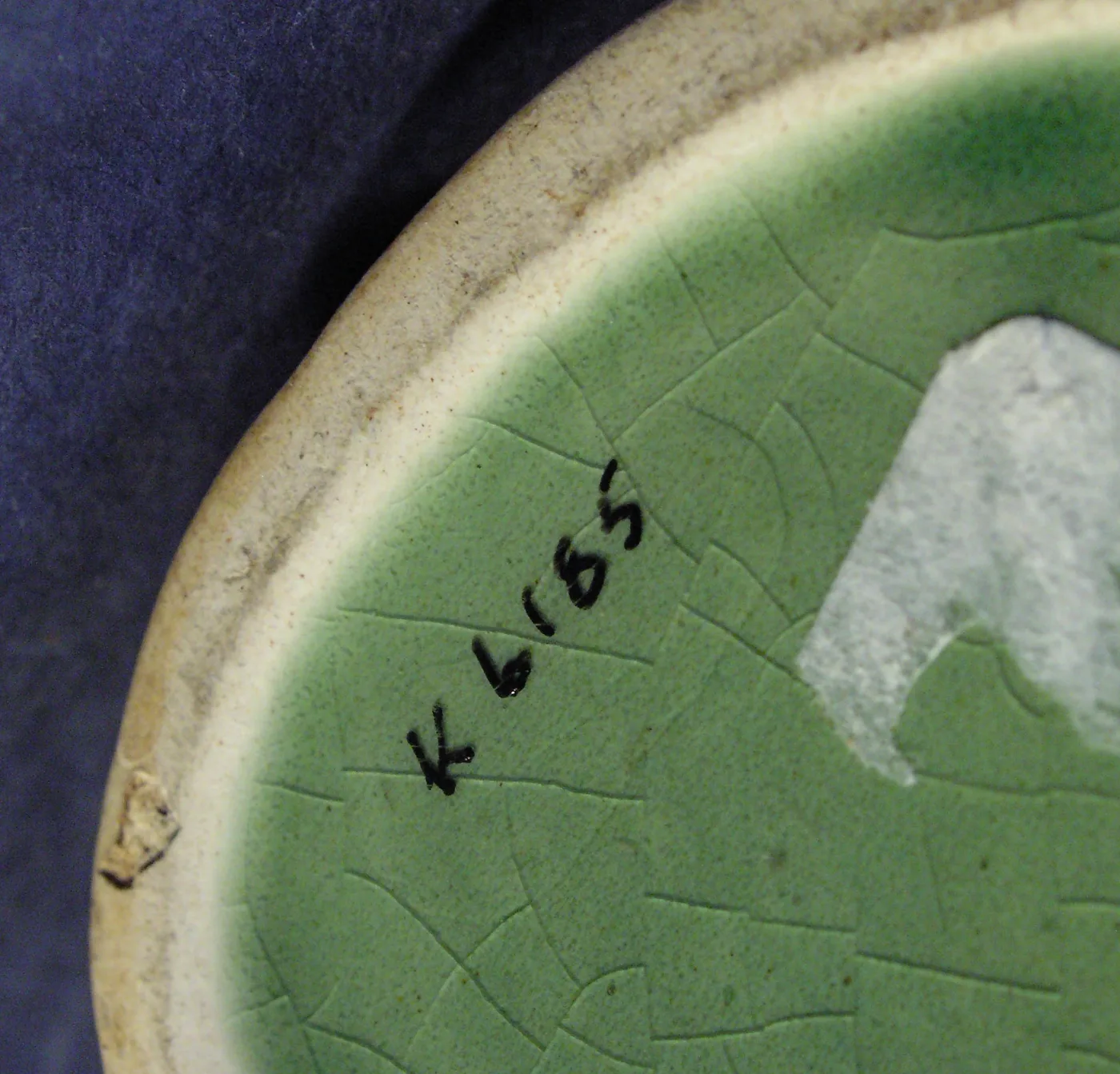 Close view of the unglazed and glazed underside of a green jug, the glaze covered in a fine network of crazing lines, with a handwritten accession number in black ink