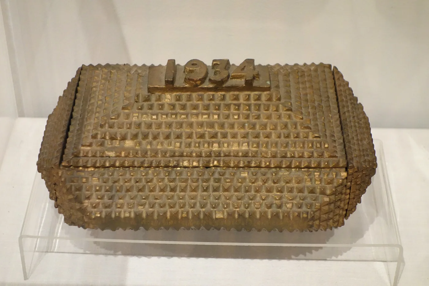 Gold-painted tramp art box covered in hundreds of tiny uniform pyramid chips arranged in rows, with the date 1934 carved in raised block figures on the lid