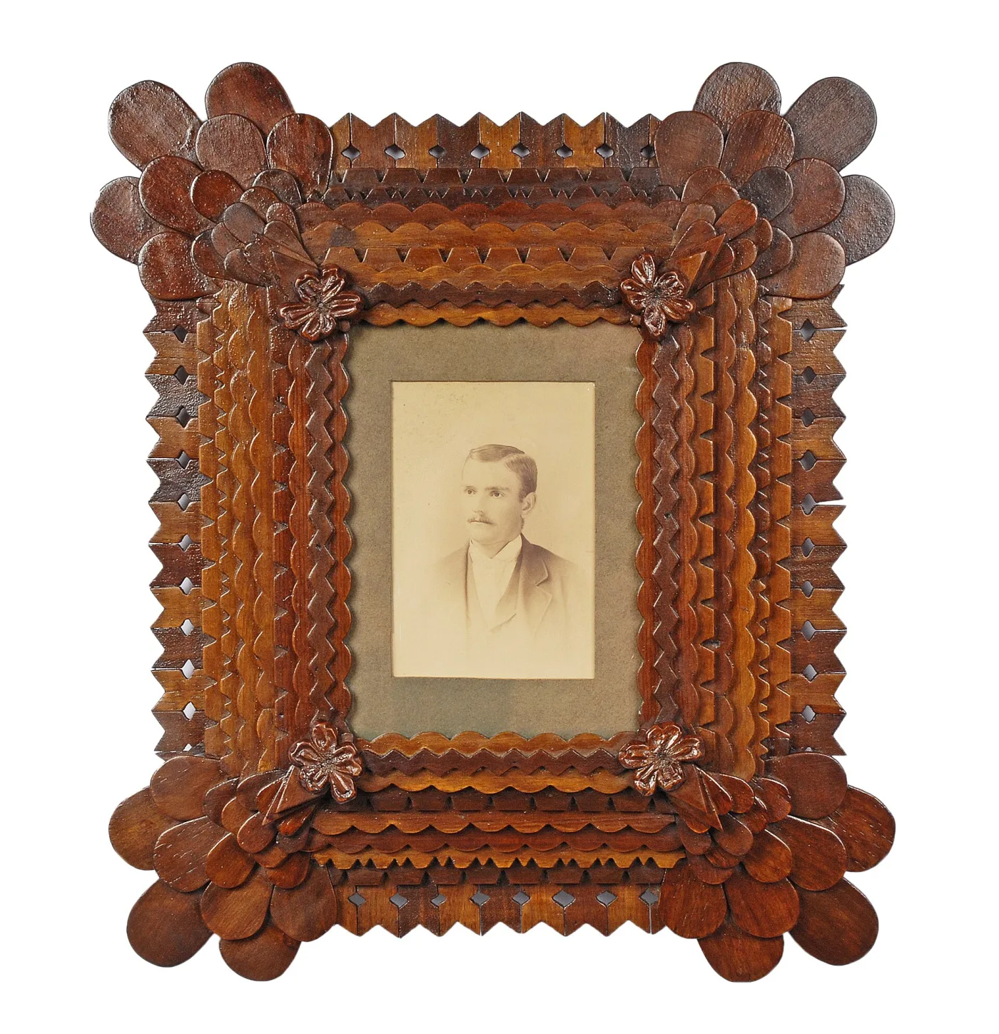 Deep tramp art photograph frame of several notched wooden tiers, with rounded petal-shaped discs fanned at the corners and small carved flowers, holding a sepia portrait of a moustached young man