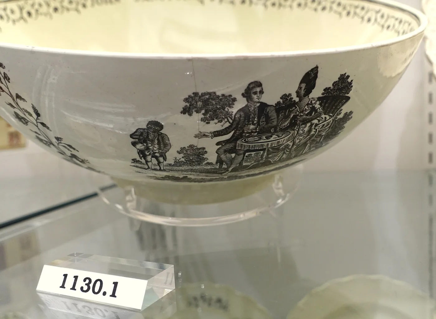 Wide creamware punch bowl printed in black with a figure at a table under a tree, an inscription running around the rim
