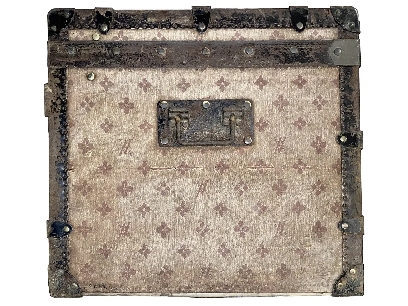 Corner of a travelling trunk covered in a pale jacquard-woven canvas patterned with repeated interlaced initials, with a scuffed brass lock plate and dark leather binding at the edges