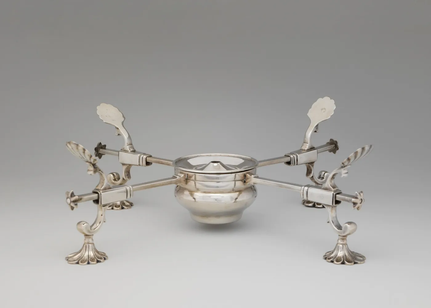 Silver dish cross with four sliding arms on scrolled feet, four shaped rests and a covered spirit burner at the centre